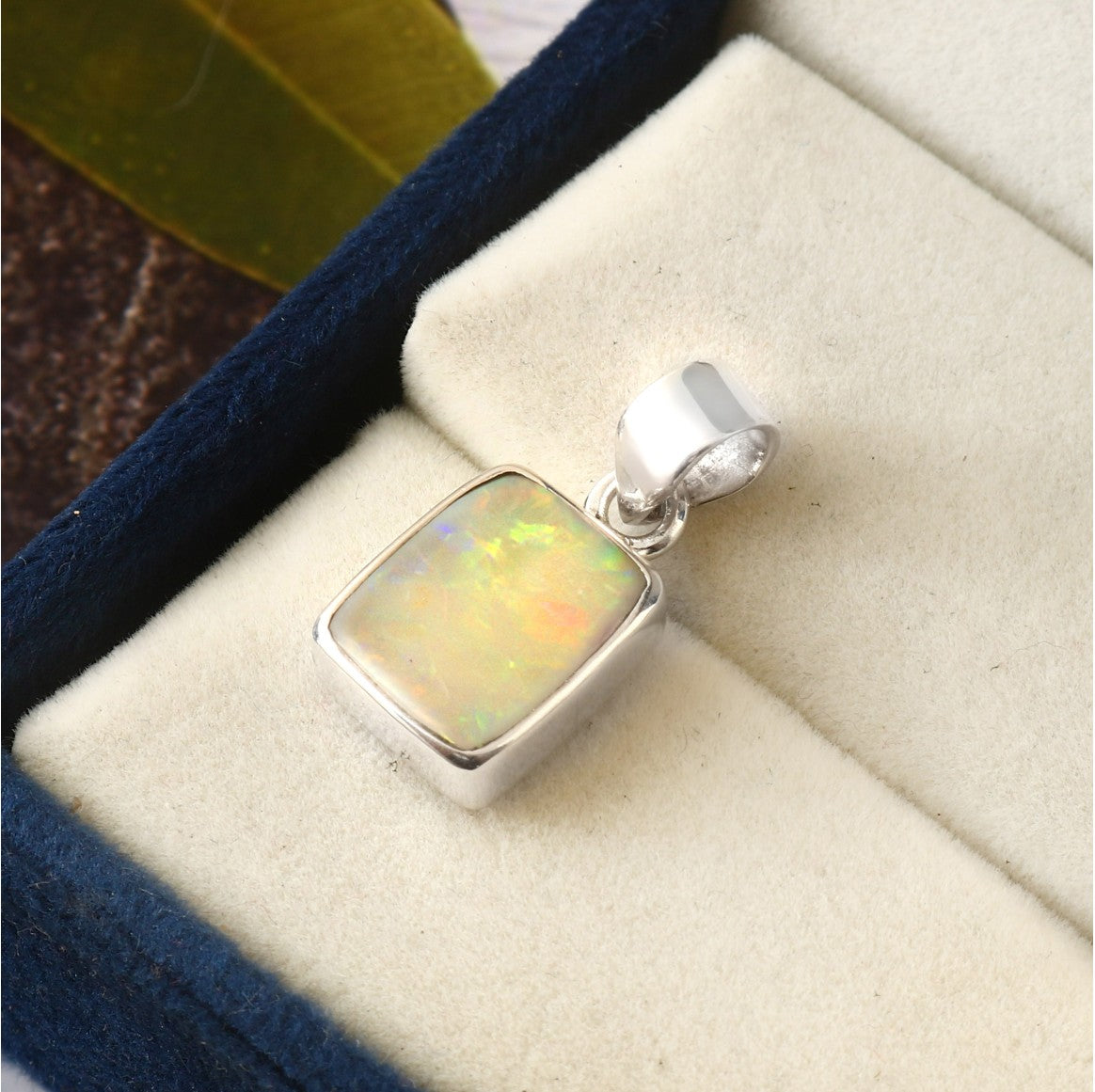Opal pendant in silver setting on a beige cushion with blue velvet border